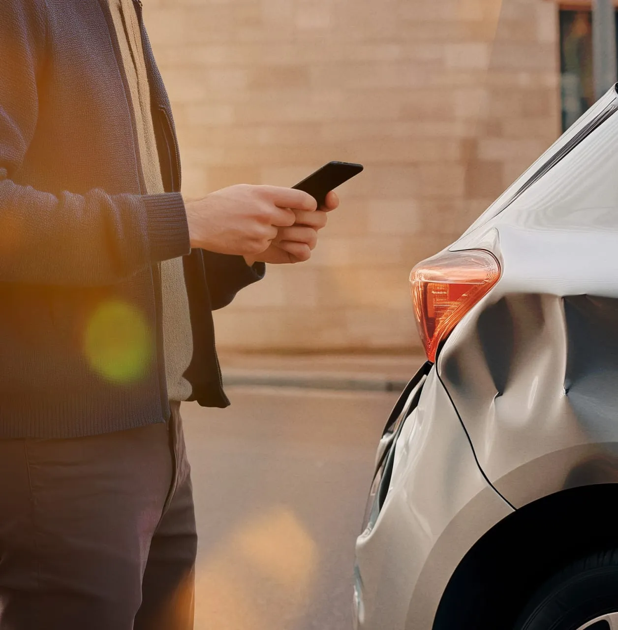 A man is using his phone to make a call while standing next to his car